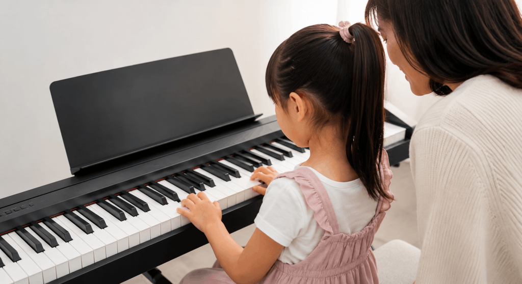 Batang babae na nag-aaral sa digital piano habang ginagabayan ng magulang sa komportable at simpleng home setup.